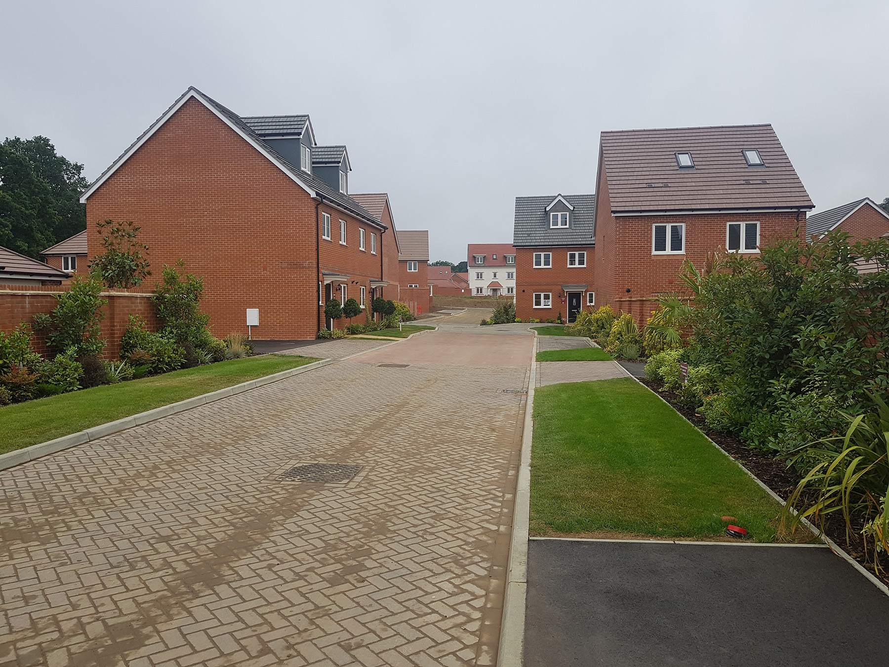 Block-paved estate road with grass verges between new brick homes at Blue Mountain, Binfield